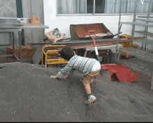 a little boy is playing with a shovel in a room with a yellow cart with a bag of cement in it