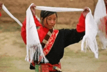 a young girl in a red and black dress is holding a white scarf around her neck .