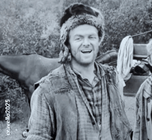 a man wearing a fur hat and a plaid shirt is smiling in a black and white photo