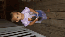 a little girl wearing a frozen shirt stands on a wooden deck