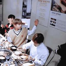 a group of young men are sitting at a table eating food with a poster on the wall that says ' korean language '