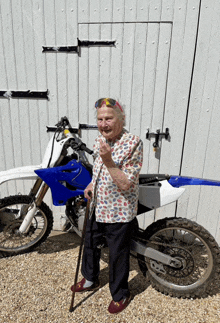 an elderly woman is standing next to a dirt bike and giving a thumbs up