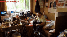 a man sits on a bed in a messy room with a sign on the wall that says omeczny czlowiek