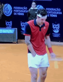 a man in a red shirt and white shorts is playing tennis in front of a sign that says federacao portuguesa de tenis