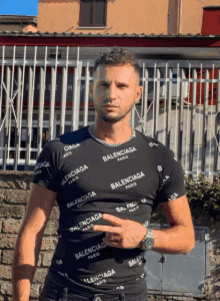 a man wearing a balenciaga t-shirt stands in front of a fence