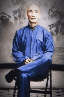 a bald man in a blue shirt sits on a chair