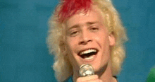 a man with red hair is singing into a microphone while smiling .