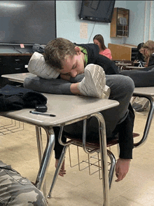 a boy is sleeping on a desk in a classroom with a dell monitor behind him