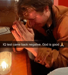 a man sitting at a table with his hands folded in prayer with the caption iq test came back negative god is good .