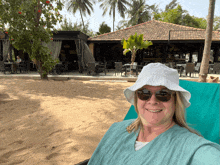 a woman wearing a white hat and sunglasses sits in a chair on a beach