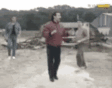 a man in a red jacket is dancing in a field while two other people watch .