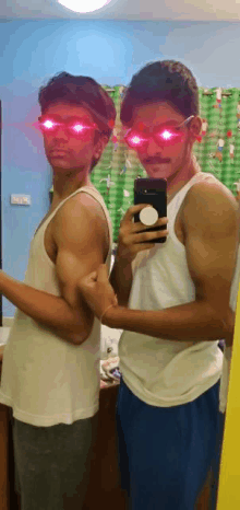 two men are taking a picture of themselves in a mirror . one of the men is wearing red glasses .