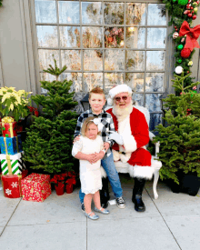 three children pose for a picture with santa claus in front of christmas trees