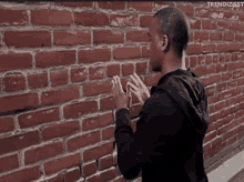 a man is standing in front of a red brick wall .