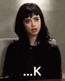 a woman with black hair and bangs is sitting at a table .