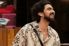 a man with a beard wearing a floral shirt is laughing with his eyes closed .