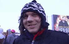 a man wearing a black and white hat is smiling in front of a billboard that says ' sander ' on it