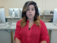 a woman in a red shirt is standing in front of a computer monitor