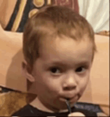 a young boy is holding a fork in his mouth and looking at the camera .