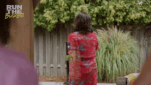 a woman in a red dress is standing in front of a fence with the words run the burbs on the bottom