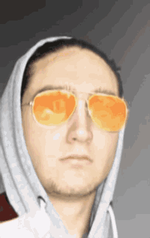 a man wearing a grey hoodie and orange sunglasses is making a funny face