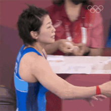 a woman in a blue tank top is sitting at a table with her arm outstretched in front of her .