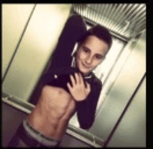 a young man is taking a picture of himself in an elevator without a shirt on .