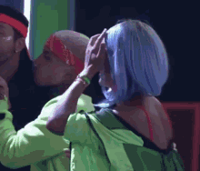 a woman in a blue wig is touching a man 's head in front of a mirror