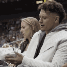 a man and a woman are sitting in the stands at a basketball game and the man is wearing a white jacket