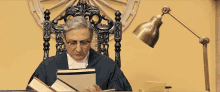 a man in a judge 's robe sits in a chair reading a book