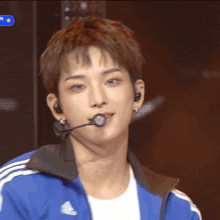 a young man wearing a blue adidas jacket and ear buds