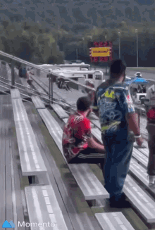 a group of people sitting on bleachers at a race track with the word momento in the bottom right corner