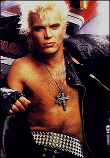 a shirtless man wearing a cross necklace and a studded belt stands in front of a suzuki motorcycle