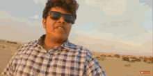 a young man wearing sunglasses and a plaid shirt is standing in the desert .