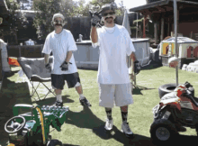 two men standing next to each other in a backyard with a toy tractor and a honda atv in the background