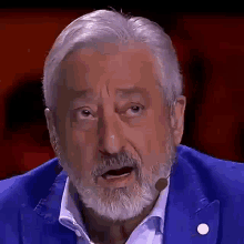 a man with a beard and a blue jacket is talking into a microphone .