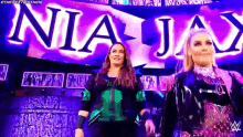 two women are standing next to each other in front of a large sign that says nia jay .