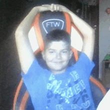 a young boy in a blue shirt is sitting in a chair with his arms over his head .