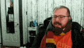 a man with glasses and a scarf around his neck is wearing an orange shirt that says ' nm ' on it
