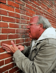 a man is leaning against a brick wall with his hands on it .