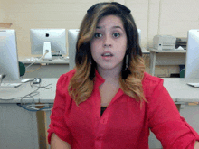 a woman in a red shirt is sitting in front of a computer monitor