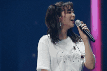 a woman singing into a microphone wearing a white shirt that says twice