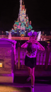 a girl wearing disney ears stands in front of a large castle