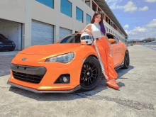 a woman holding a helmet stands next to an orange car with the word bride on the side