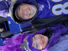 a man wearing a ravens jersey lays next to a woman wearing purple