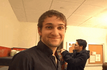 a man in a black shirt is smiling in front of a bulletin board that says ' a ' on it