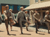 a group of men in suits and hats are dancing in front of a building with a sign that says dupont