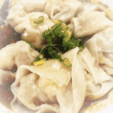 a close up of a bowl of wonton soup with green onions