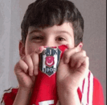 a young boy is covering his face with a red shirt that says bjk 1903