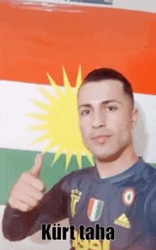 a man in a soccer jersey is giving a thumbs up in front of a kurdish flag .